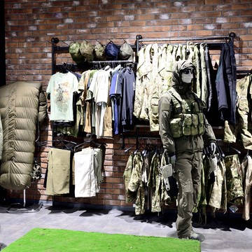 На фото одежда в стиле милитари (поло, кепки, футболки, брюки, сумки и рюкзаки), спальный мешок SnugPack, на манекене тактический костюм и разгрузочный жилет